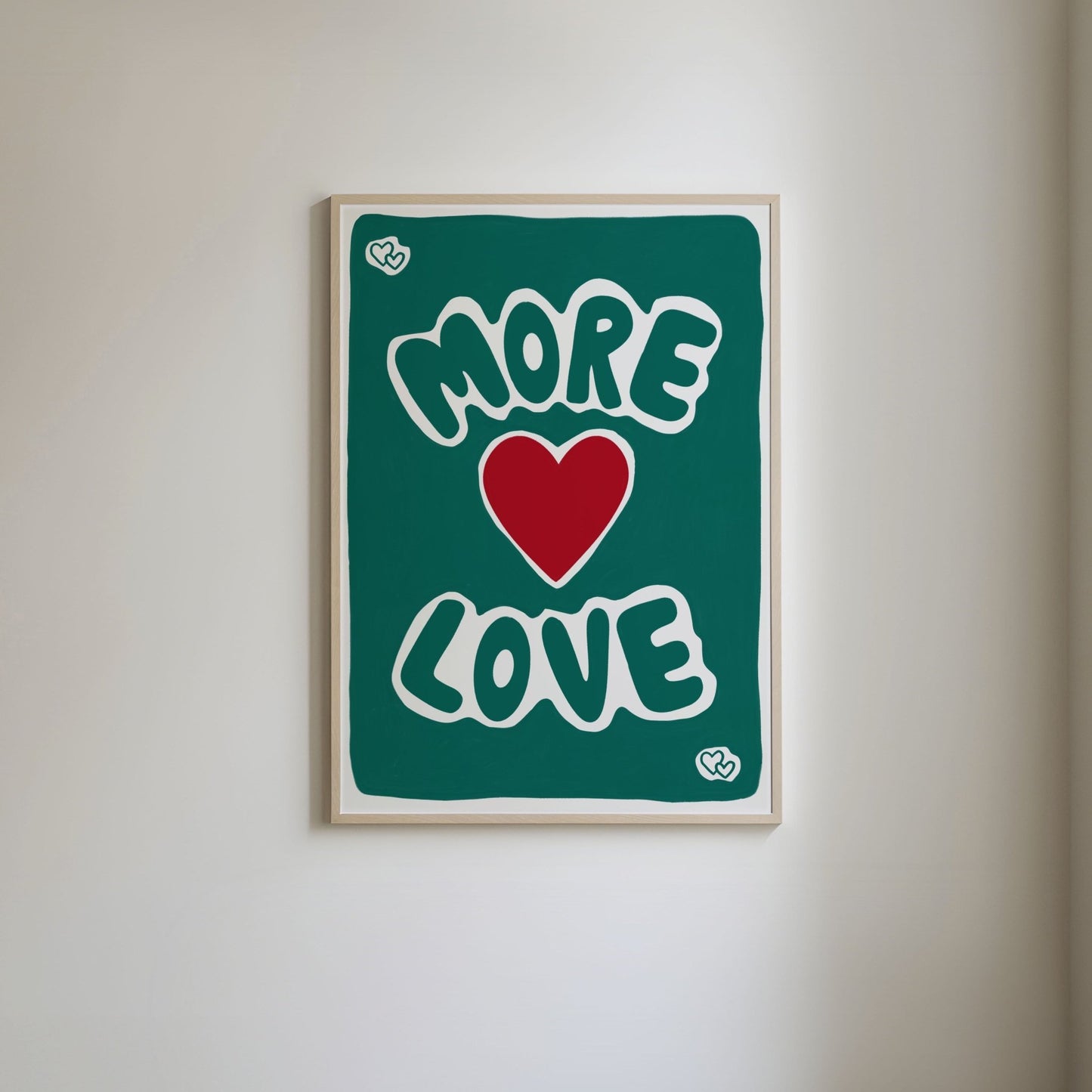 Art print with a green painted background, featuring bold 'More Love' text in vibrant lettering, with a bright red heart in the center and small green hearts in each corner."