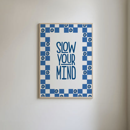 Typography print with 'Slow your mind' in blue, surrounded by a blue and white checkered border featuring blue evil eye illustrations.